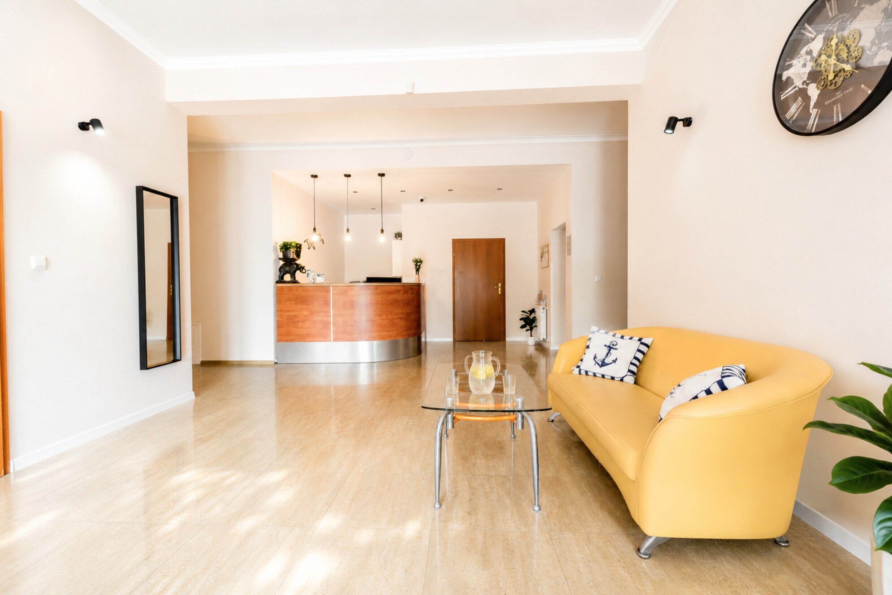 Una sala de estar moderna con un sofá amarillo, una mesa de centro de vidrio y un mostrador de recepción al fondo.