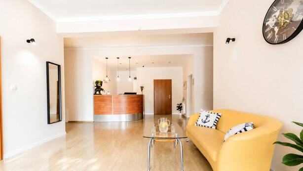 Een moderne woonkamer met een gele bank, een glazen salontafel en een receptiebalie op de achtergrond.