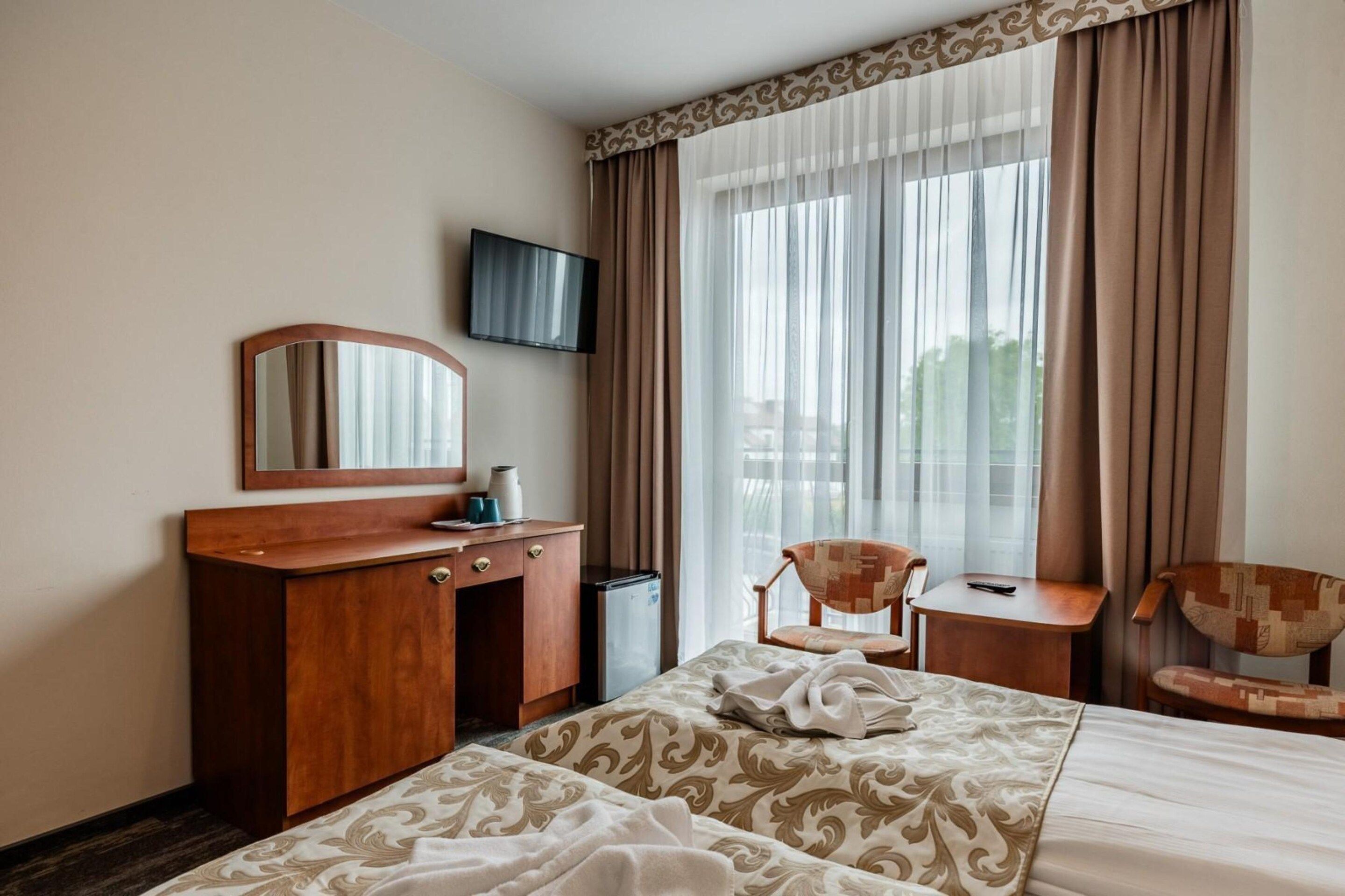 Een hotelkamer met een bed, een bureau, een stoel, een televisie en een raam met gordijnen.
