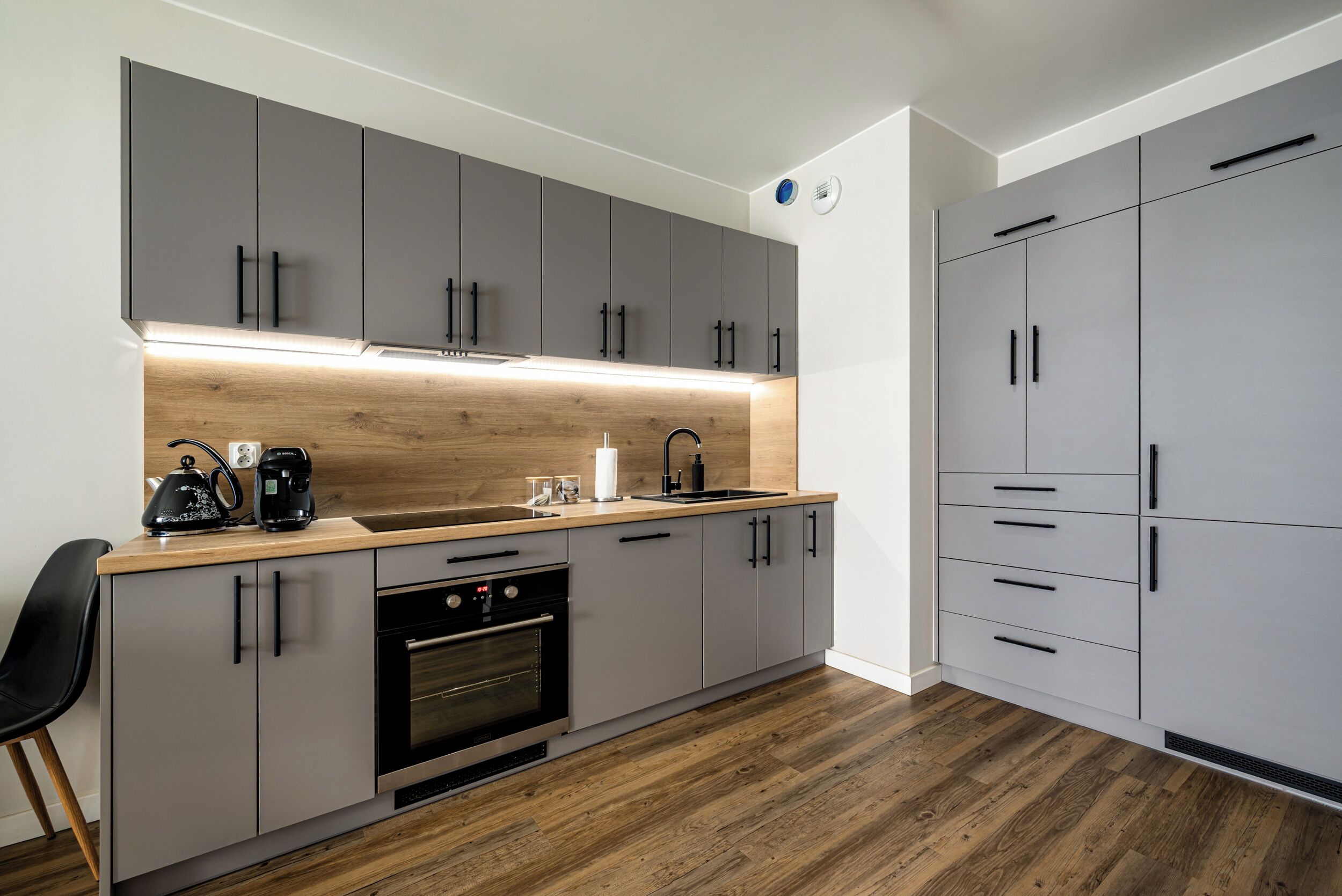 A modern kitchen with grey cabinets, a wooden countertop, a built-in oven, and a sink.