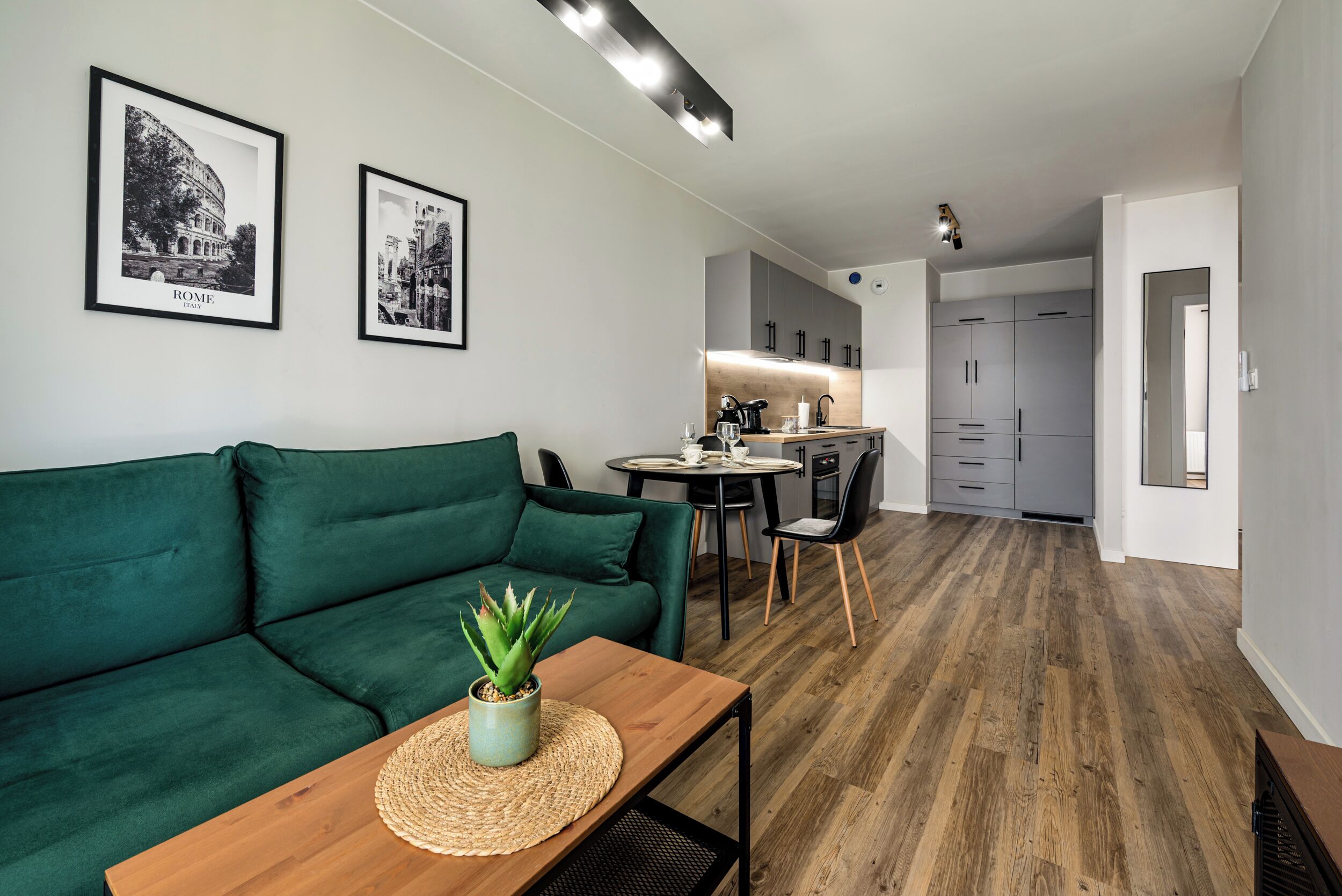 Een moderne woonkamer met een groene bank, een salontafel met een plant en een eetgedeelte met een tafel en stoelen.