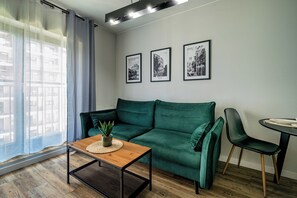 Una sala de estar moderna con un sofá verde, una mesa de centro de madera con una planta y tres cuadros en la pared.