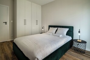 Un dormitorio con cama, armario, mesita de noche con lámpara y una mesita auxiliar redonda también con lámpara.