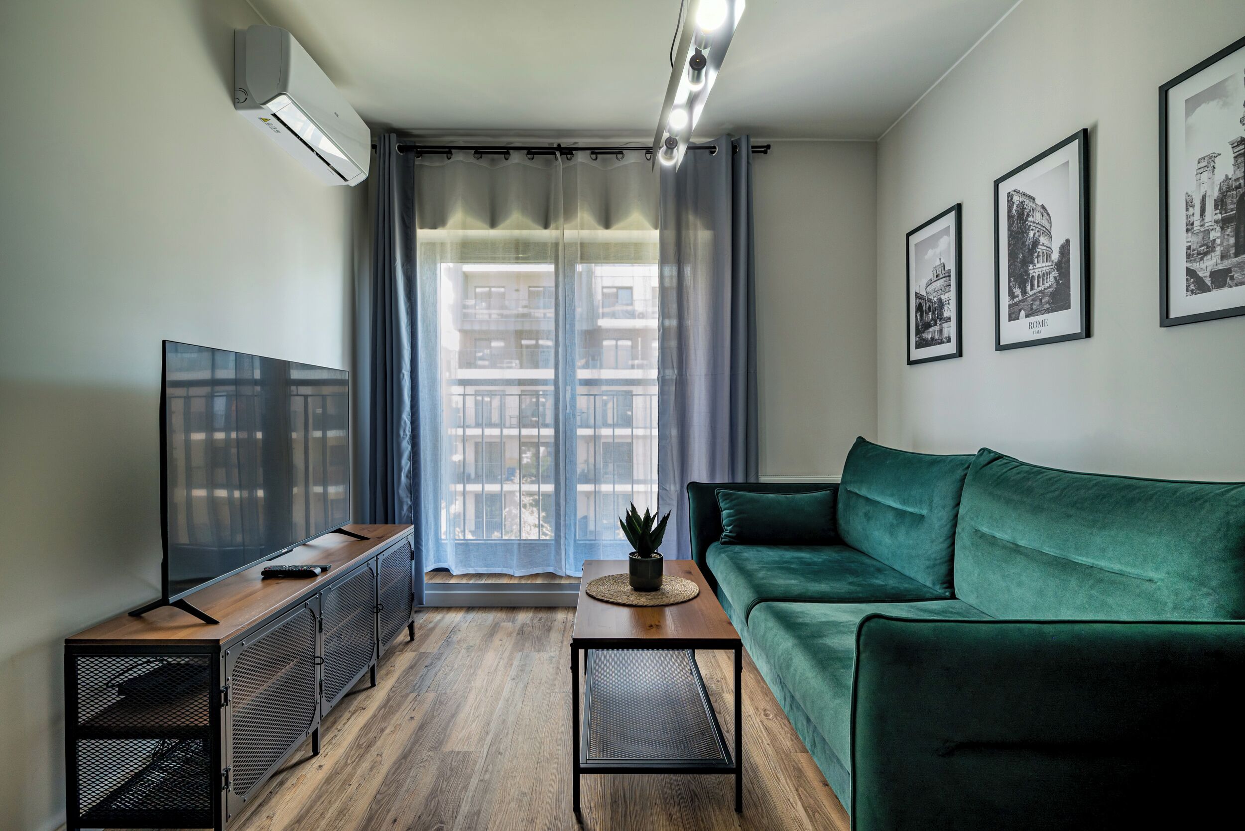 Een moderne woonkamer met een flatscreen televisie, een groene bank, een salontafel en een potplant.