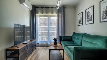 Een moderne woonkamer met een flatscreen televisie, een groene bank, een salontafel en een potplant.