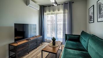 Een moderne woonkamer met een flatscreen televisie, een houten salontafel, een groene bank en een potplant.