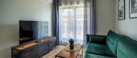 A modern living room with a flat-screen TV, a wooden coffee table, a green sofa, and a potted plant.