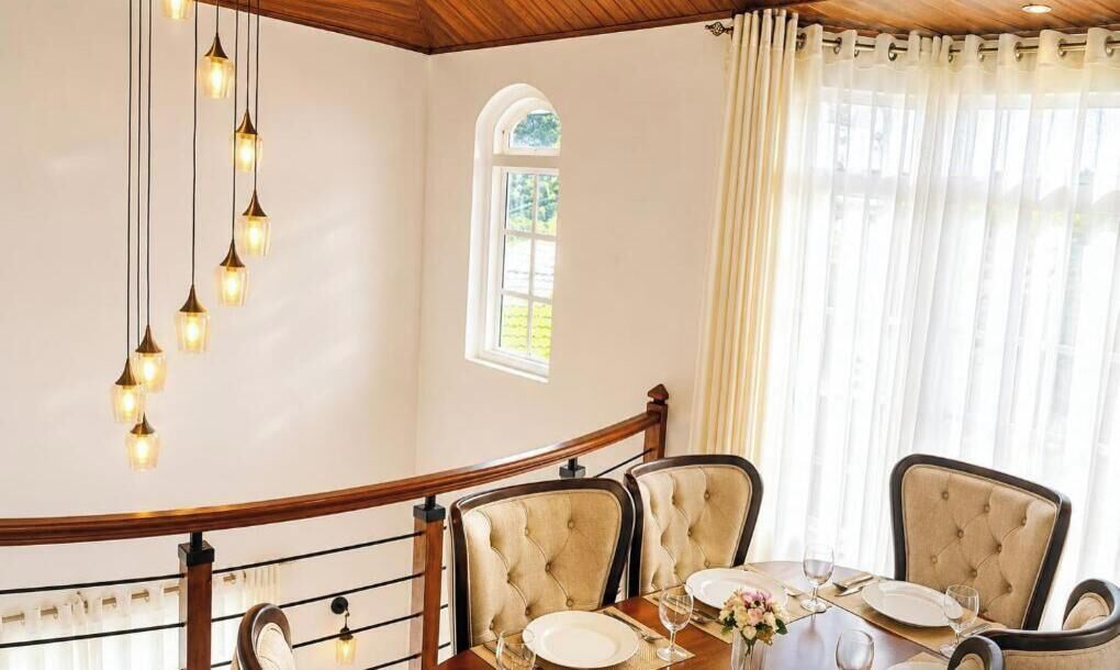 Uma área de jantar com uma escada de madeira curva, uma mesa posta para quatro pessoas e um candelabro.