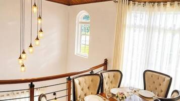 Uma área de jantar com uma escada de madeira curva, uma mesa posta para quatro pessoas e um candelabro.