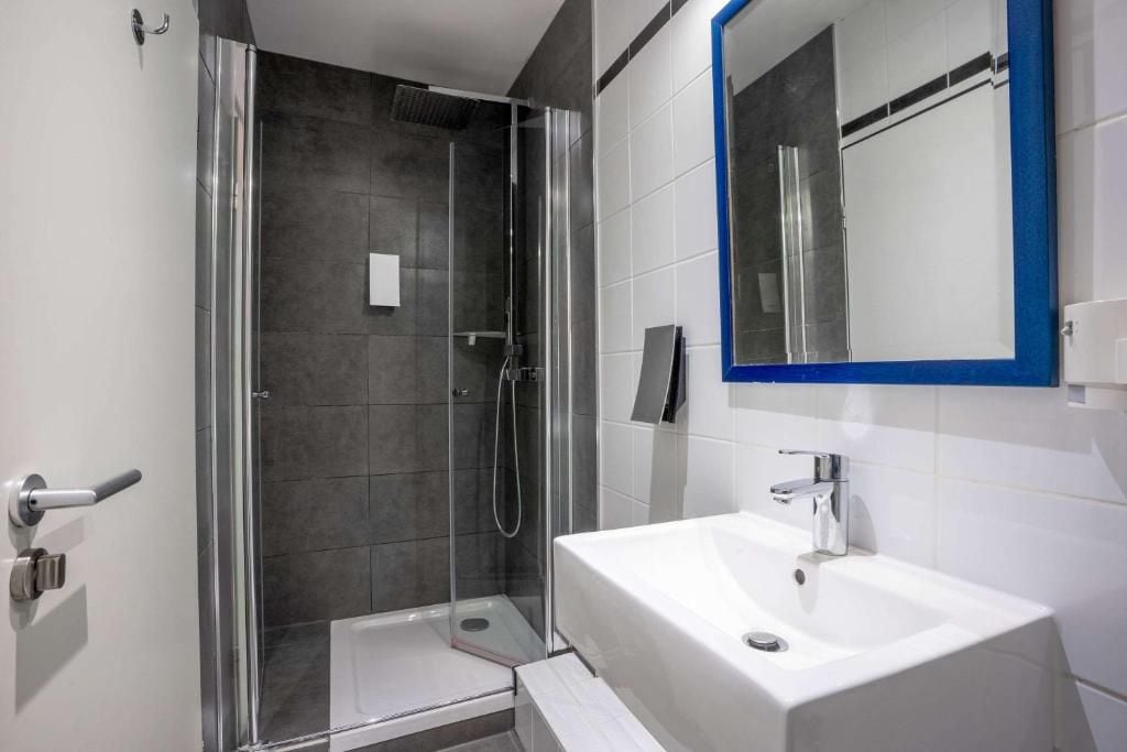 Un baño moderno con ducha de vidrio, lavamanos blanco y espejo con marco azul.