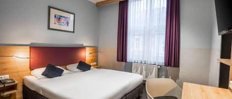 A hotel room with a bed, bedside table, chair, and a TV.