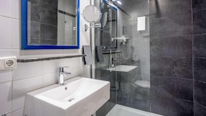 Un baño moderno con un lavabo blanco, un espejo con marco azul y una zona de ducha con mampara de vidrio.