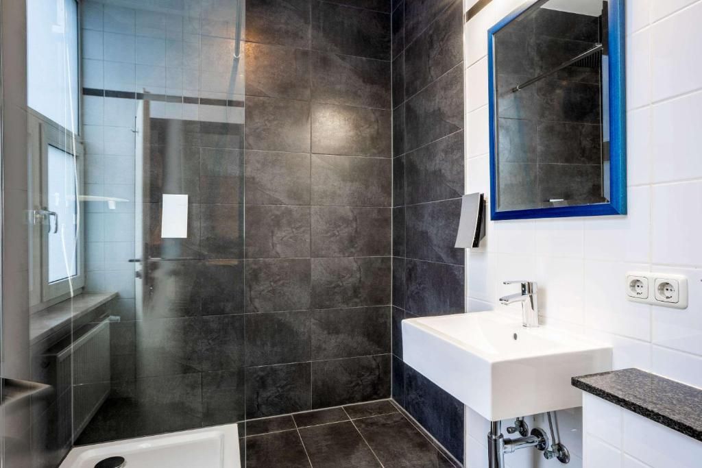 Un baño moderno con ducha envuelta en vidrio, un lavabo blanco y un espejo con marco azul.