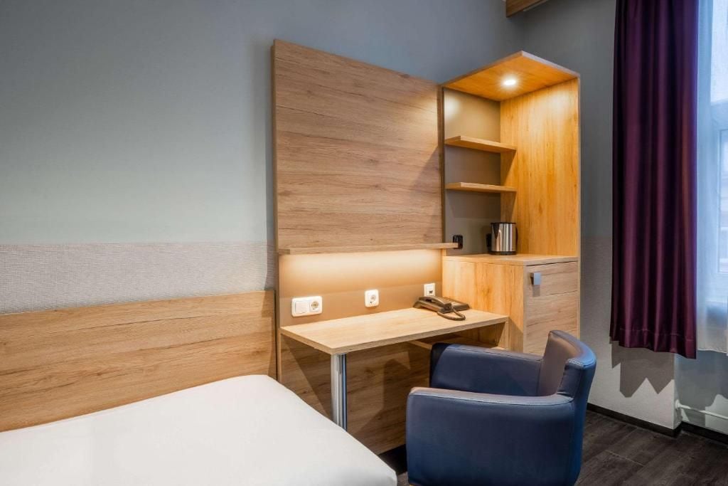 Una habitación de hotel con cama, escritorio con silla, aparador de madera y ventana con cortinas.