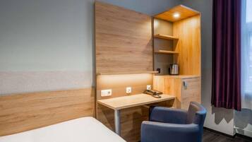 Una camera d'albergo con un letto, una scrivania con una sedia, un armadio in legno e una finestra con tende.