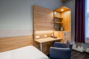 A hotel room with a bed, a desk with a chair, a wooden cabinet, and a window with curtains.