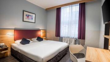 Une chambre d’hôtel avec un lit, une table de chevet, une chaise et un téléviseur.