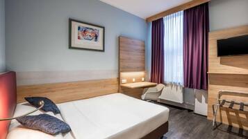 Una habitación de hotel con cama, escritorio, silla, televisión y ventana con cortinas.