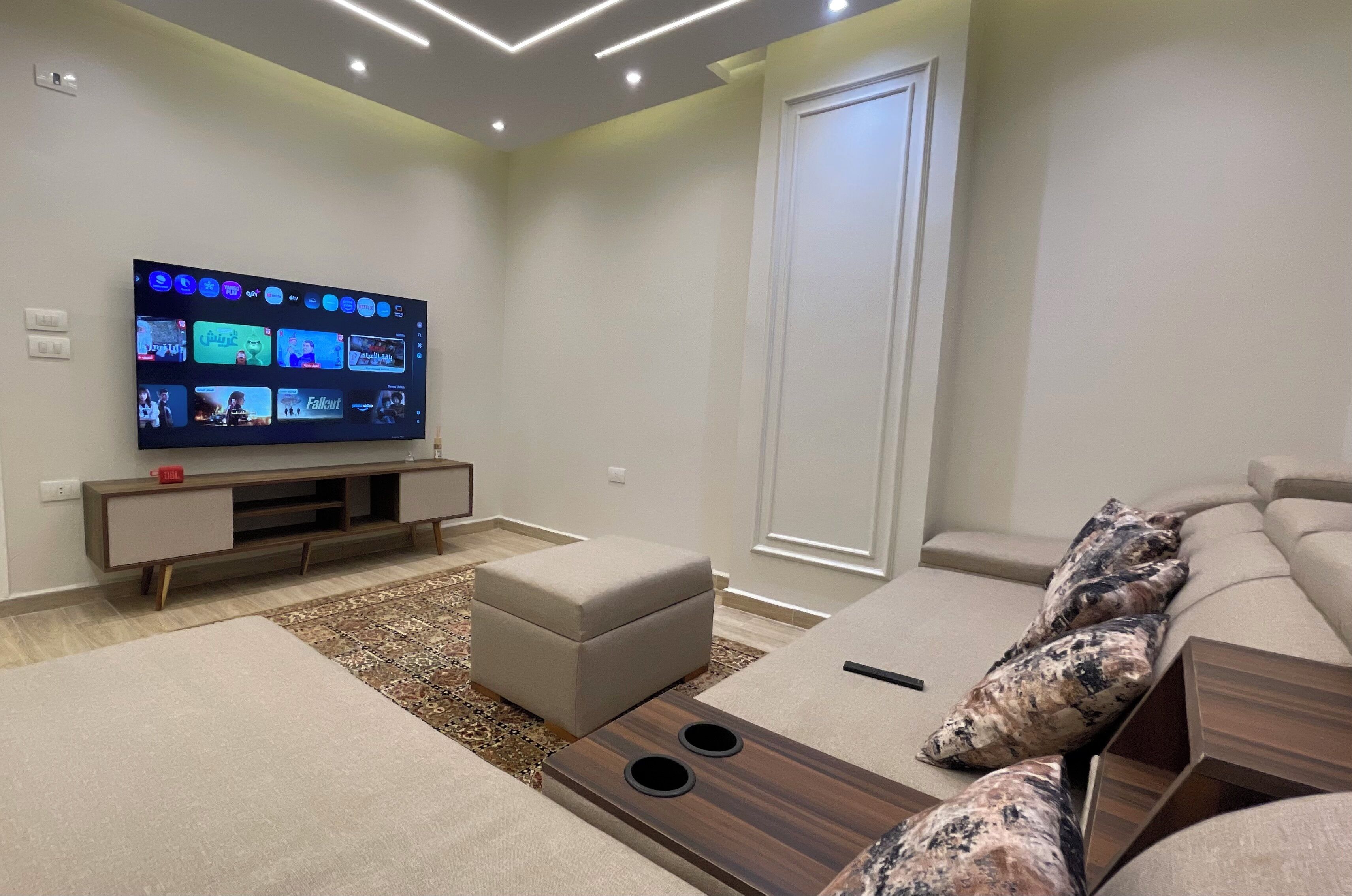 A modern living room with a flat-screen TV, a sofa, an ottoman, and a coffee table.