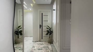 A hallway with a patterned carpet, a door with a black handle, and a potted plant on each side.