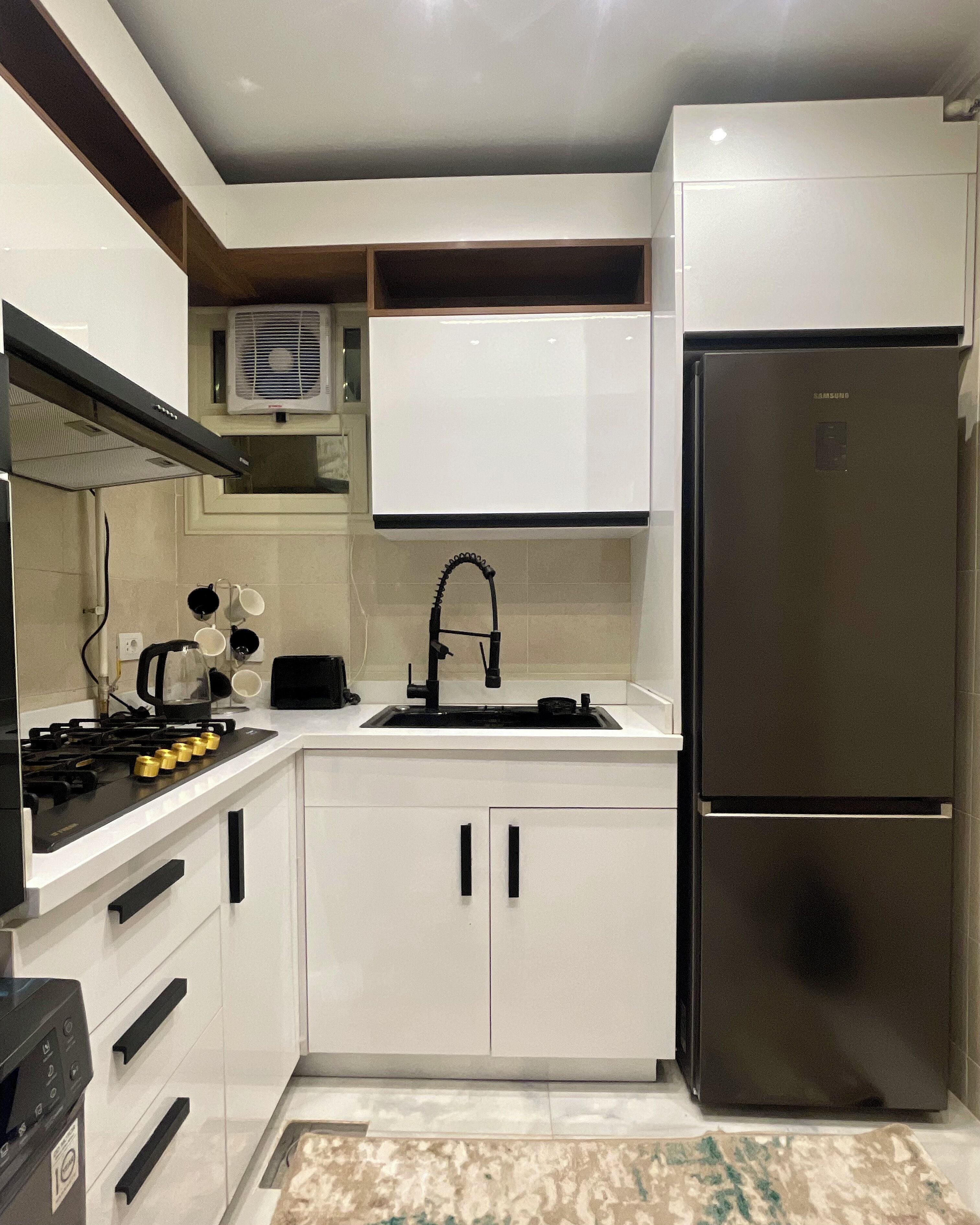 A compact kitchen with white cabinetry, a stainless steel refrigerator, a gas stove, and a built-in oven.