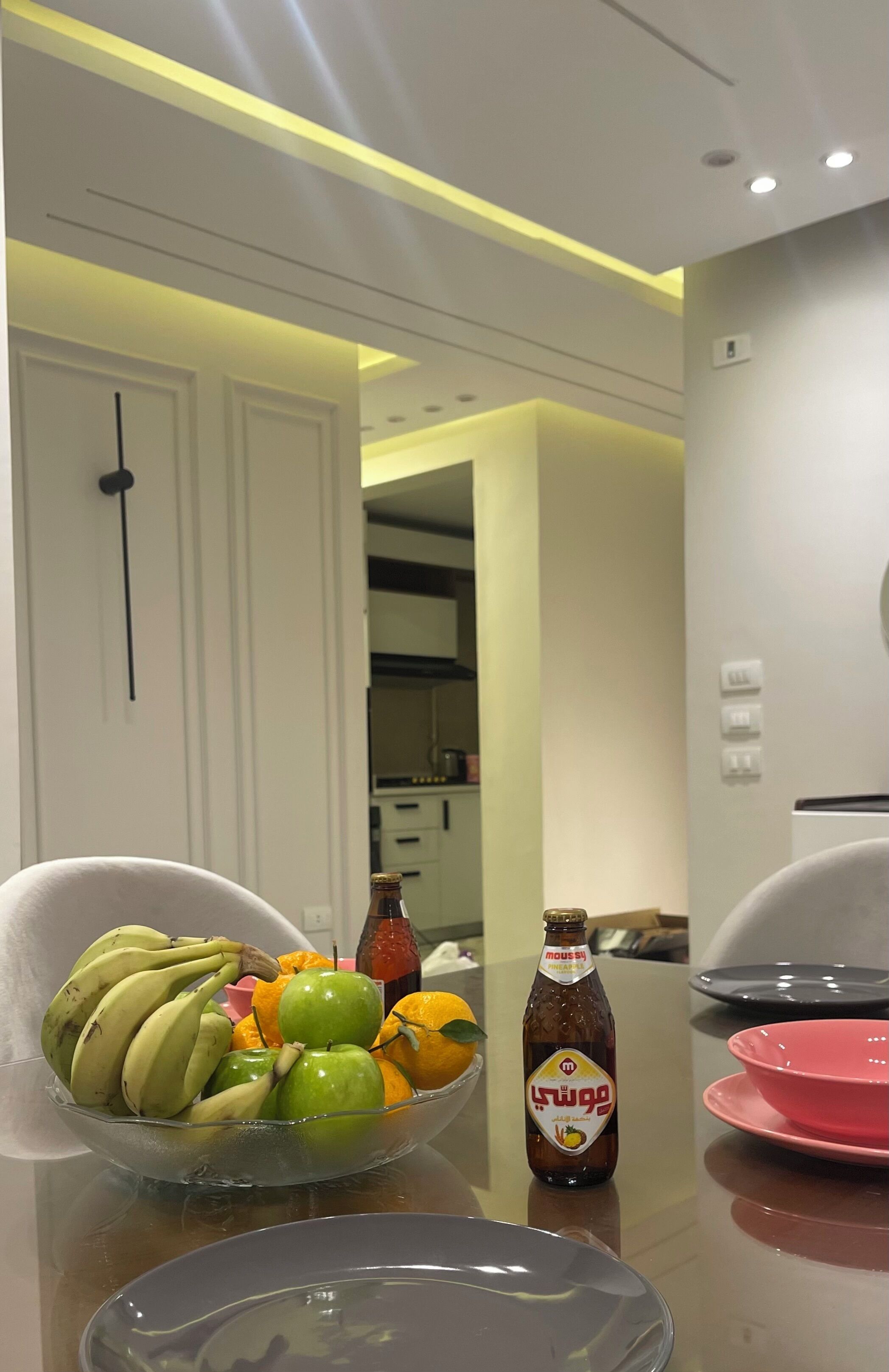 A dining table with a fruit bowl, a bottle, and plates.