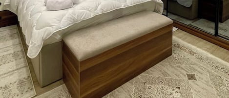 A modern bedroom with a large bed, a wooden bench, a mirror, and a patterned rug.