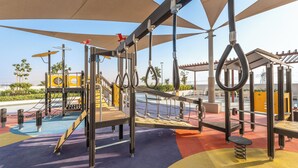 Un patio de juegos al aire libre con diverso equipo de ejercicio, incluyendo anillos, una escalera de cuerda y una estructura para escalar.