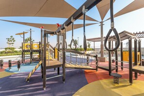 An outdoor playground with various exercise equipment, including rings, a rope ladder, and a climbing structure. - StayShort - Minutes to Downtown - Sleek Meydan Apartment with Balcony - Sleeps 4 (Dubai)