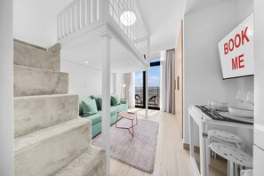 A modern interior with a staircase, a green sofa, a dining area, and a view of the outdoors. - StayShort - Minutes to Downtown - Sleek Meydan Apartment with Balcony - Sleeps 4 (Dubai)