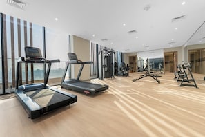 A gym with treadmills, weight machines, and a large mirror. - StayShort - Minutes to Downtown - Sleek Meydan Apartment with Balcony - Sleeps 4 (Dubai)