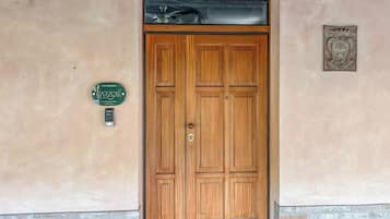 A wooden double door with a keypad lock, a green plaque with contact information, and a decorative metal plate above the door.