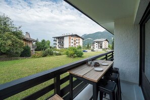 A balcony with a wooden table, a chair, and a view of a mountain and buildings. - Avenieres - Family-Friendly Getaway | 4 Guests | Megève | Balcony (Megève)