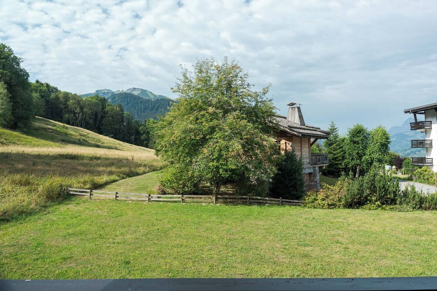 A rural property with a wooden fence, a large tree, and a building with a sloped roof.