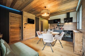 A modern kitchen with wooden accents, a dining area with a round table and chairs, and a cozy seating area with a sofa. - Avenieres - Family-Friendly Getaway | 4 Guests | Megève | Balcony (Megève)