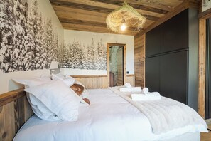 A bedroom with a wooden ceiling, a bed with white bedding, a wall with a forest mural, and a hanging light fixture. - Avenieres - Family-Friendly Getaway | 4 Guests | Megève | Balcony (Megève)