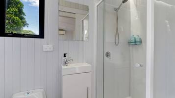 Ein modernes Badezimmer mit einer gläsernen Duschkabine, einem weißen Waschbecken mit Seifenspender und einer Toilette.