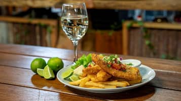 A plate of fried fish and fries with a glass of water, lime halves, and a small bowl of salad on a wooden table.