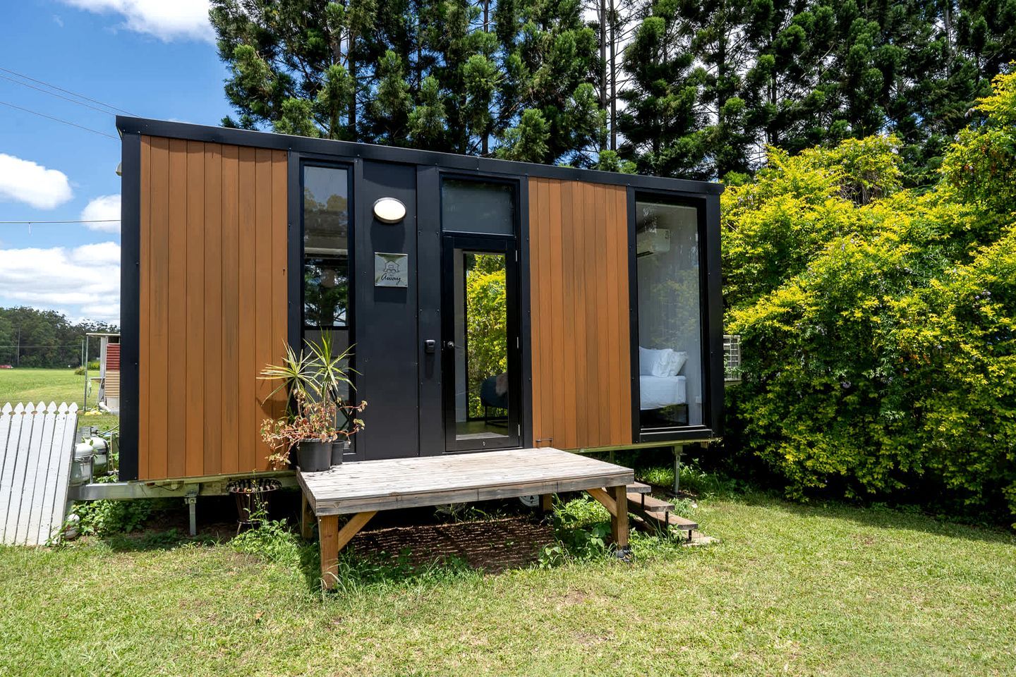 Een klein, modern vakantiehuisje met een houten gevel, een deur en een bankje buiten.