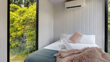 A bedroom with a large window, a bed with white bedding, a fluffy pillow, and an air conditioning unit on the wall.