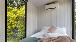 Une chambre avec une grande fenêtre, un lit avec une literie blanche, un oreiller moelleux et un appareil de climatisation fixé au mur.