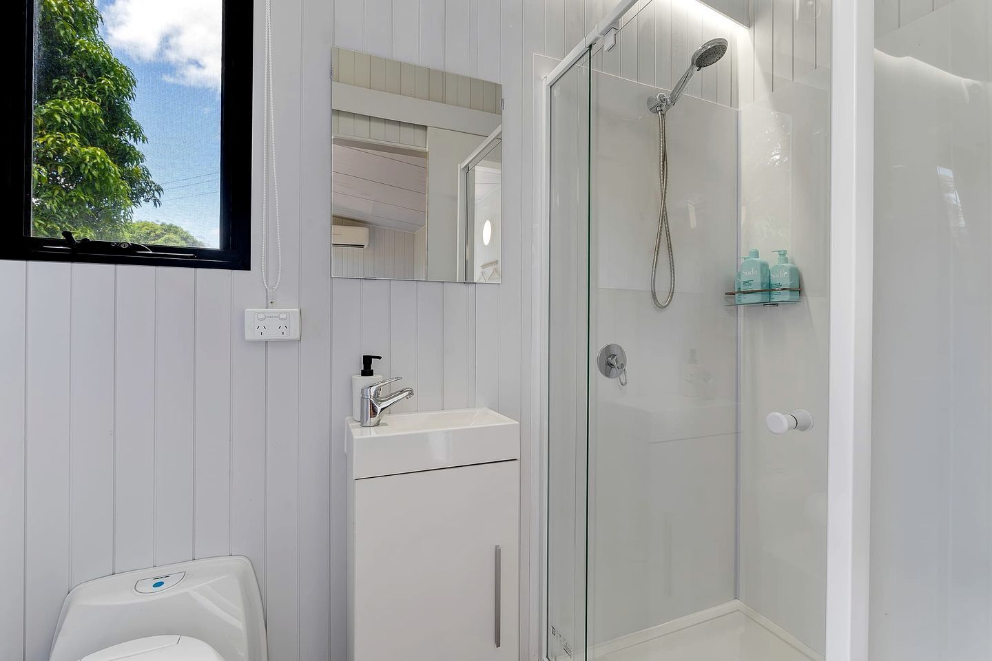 A modern bathroom with a glass-enclosed shower, a white sink with a soap dispenser, and a toilet.