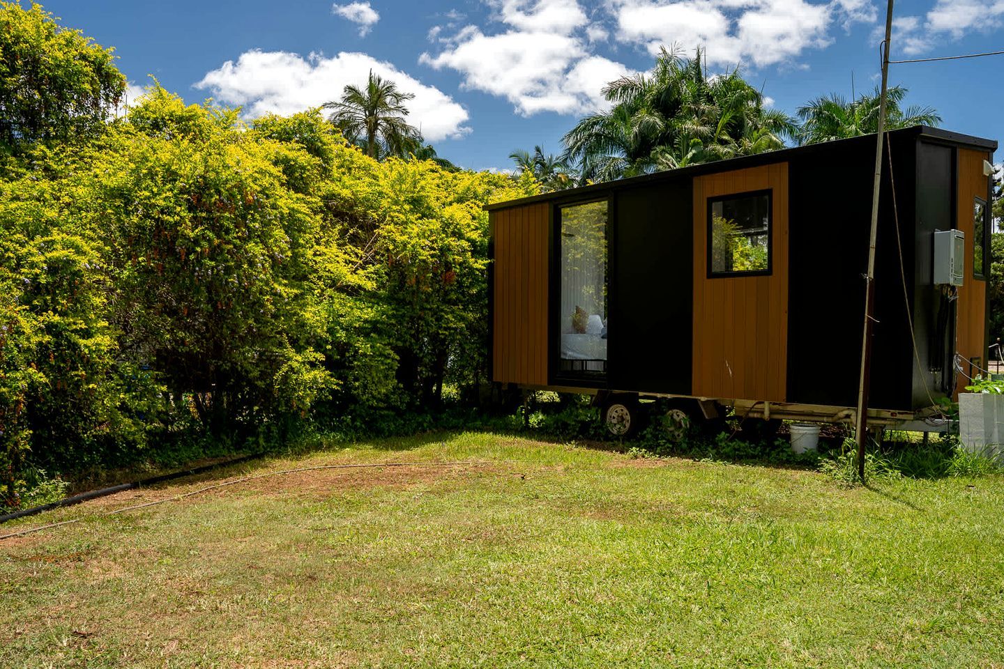 A small, single-story structure with a flat roof, situated on a grassy area with a clear sky and dense foliage in the background.