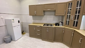 A kitchen with beige cabinets, a gas stove, and a white refrigerator. - Avenor Apartments J6 – 3-Bedroom Apartment with Living Room, Kitchen & 2 Bathrooms | Al Hamdaniyah (Jeddah)