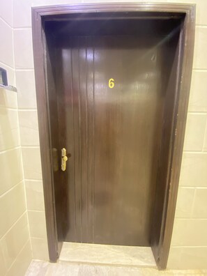 A dark wooden door with a number '6' on it, a door handle, and a tiled wall. - Avenor Apartments J6 – 3-Bedroom Apartment with Living Room, Kitchen & 2 Bathrooms | Al Hamdaniyah (Jeddah)