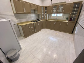 A kitchen with beige cabinets, a stainless steel sink, and a tiled floor. - Avenor Apartments J6 – 3-Bedroom Apartment with Living Room, Kitchen & 2 Bathrooms | Al Hamdaniyah (Jeddah)