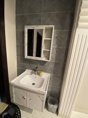 A bathroom with a white sink, a mirror, and a trash bin. - Avenor Apartments J6 – 3-Bedroom Apartment with Living Room, Kitchen & 2 Bathrooms | Al Hamdaniyah (Jeddah)