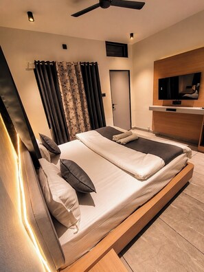 A modern bedroom with a bed, curtains, a television, and a ceiling fan.