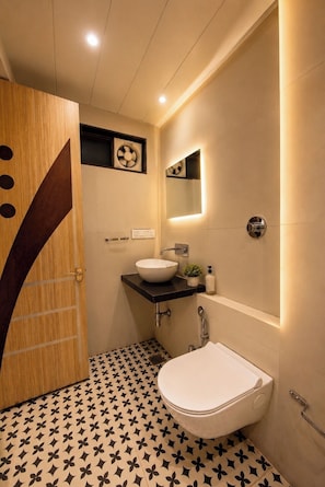 Un baño con puerta de madera, un lavabo blanco, un espejo y piso estampado.