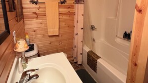A small wooden cabin bathroom with a sink, mirror, and a shower area. - Placid Cove Retreat on beautiful Lake Placid (Hayward)
